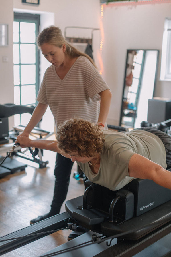 Client in a plank on the reformer box with instructor support