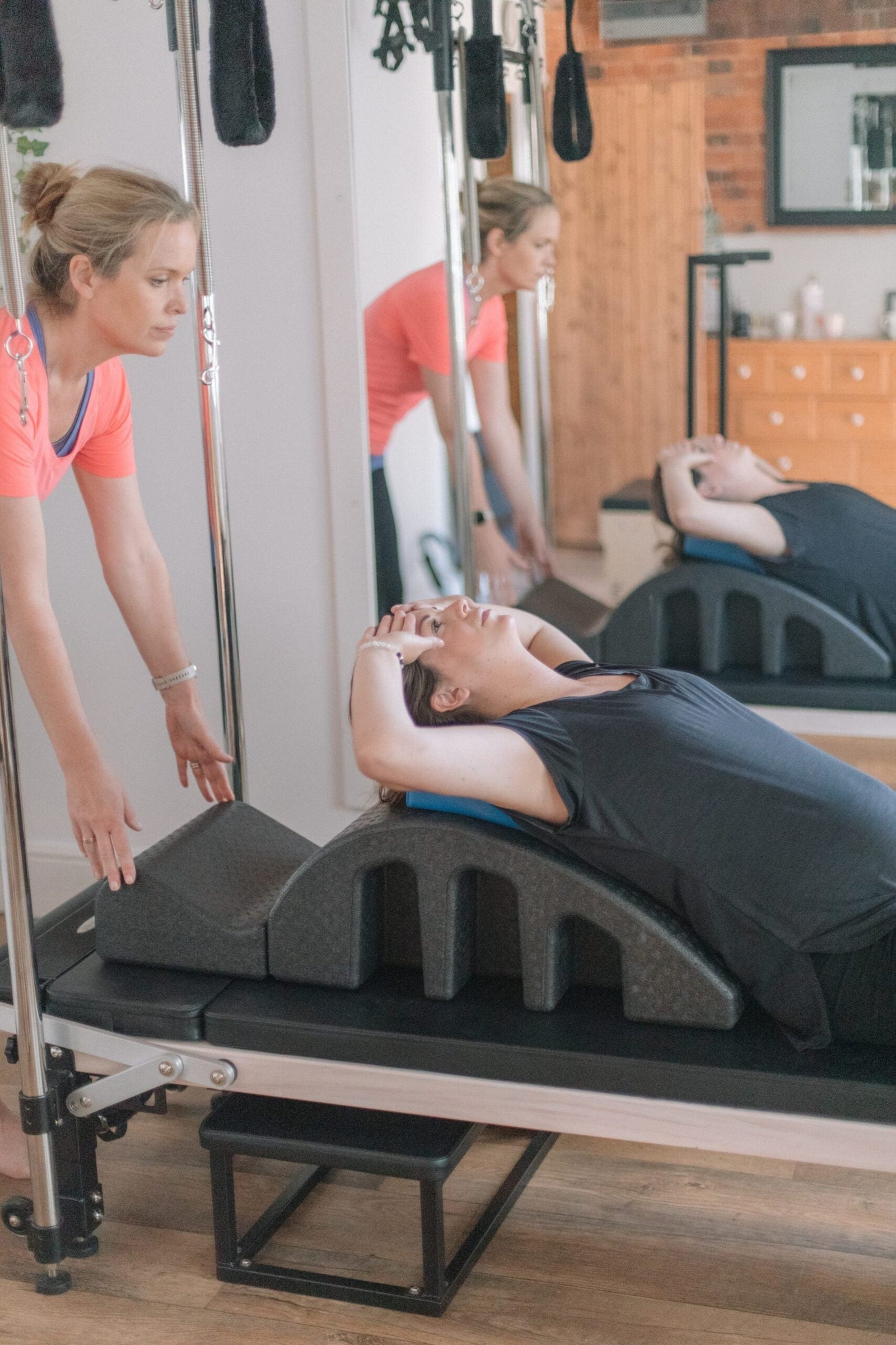 Client lying back over a spine corrector on the reformer as the instructor supports a fascia-releasing stretch