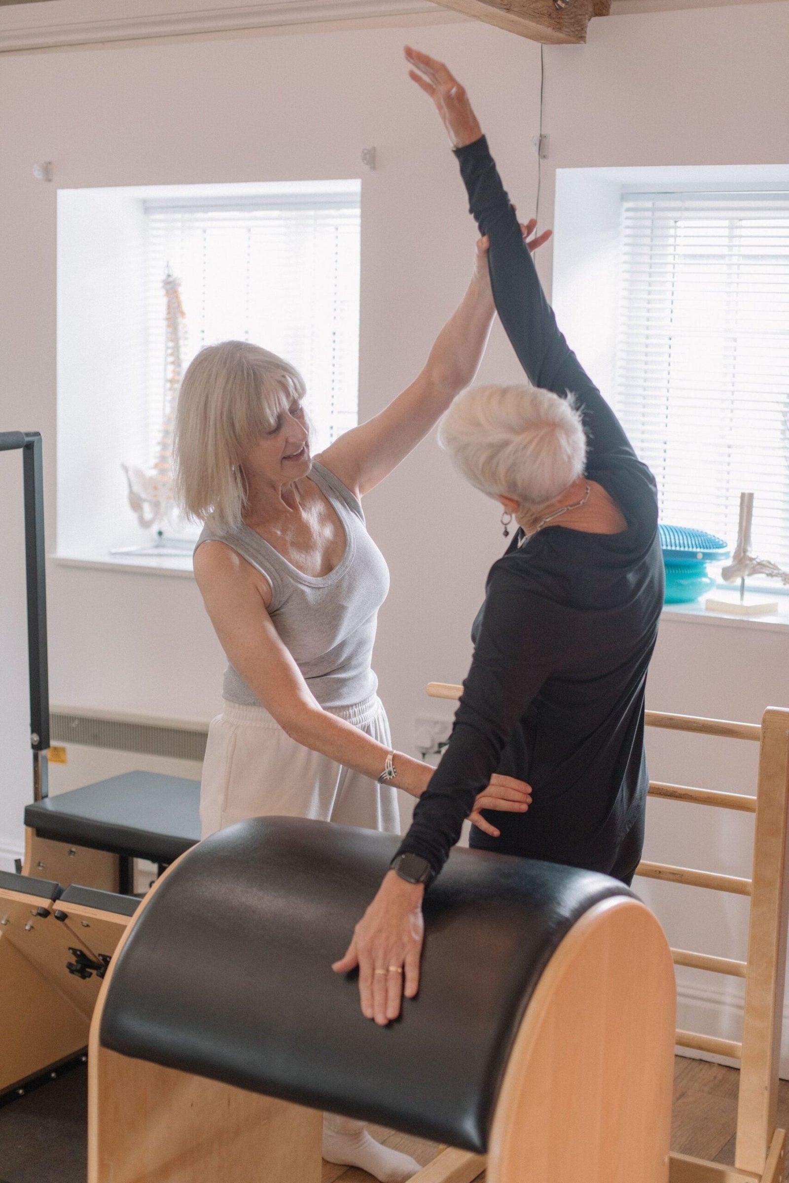 Instructor helping a client into a supported side stretch, complementing osteopathy with reformer Pilates