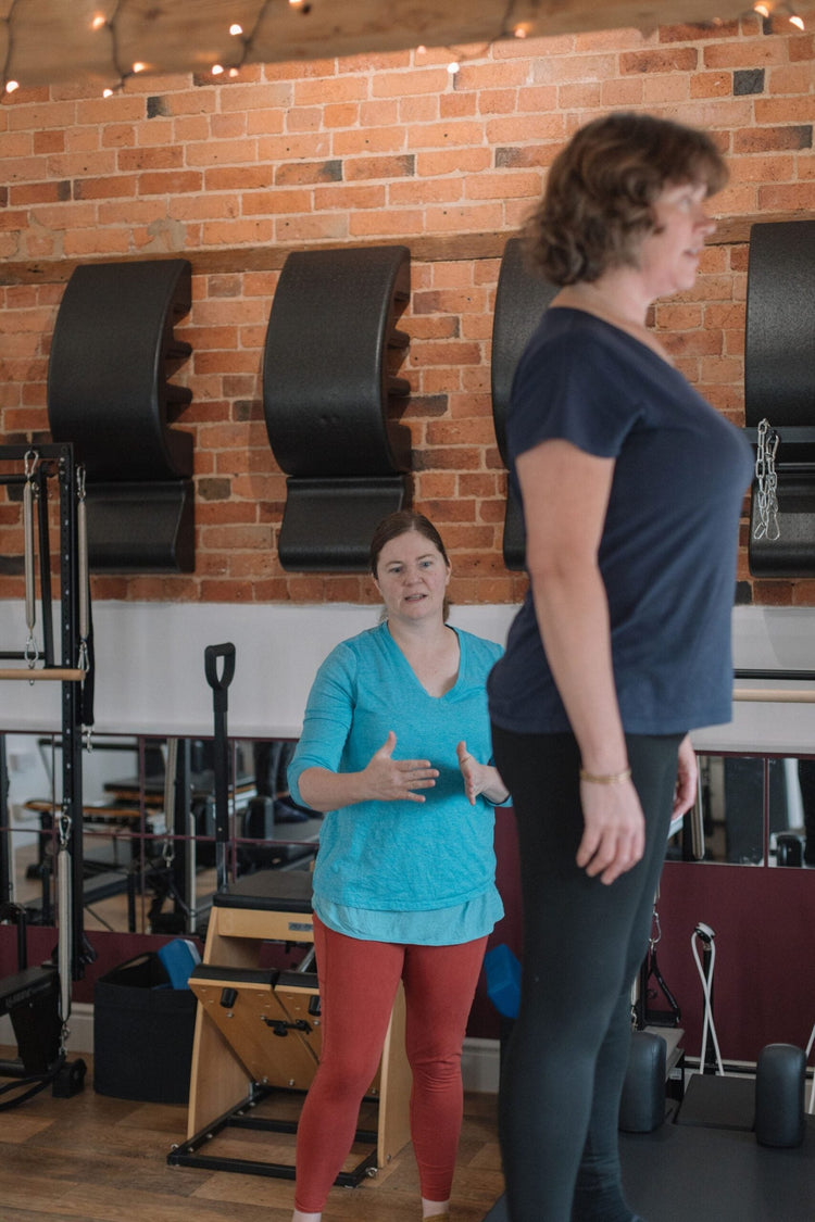 Two women in the studio discussing reformer Pilates, a joint-friendly option for seniors comparing Pilates and yoga
