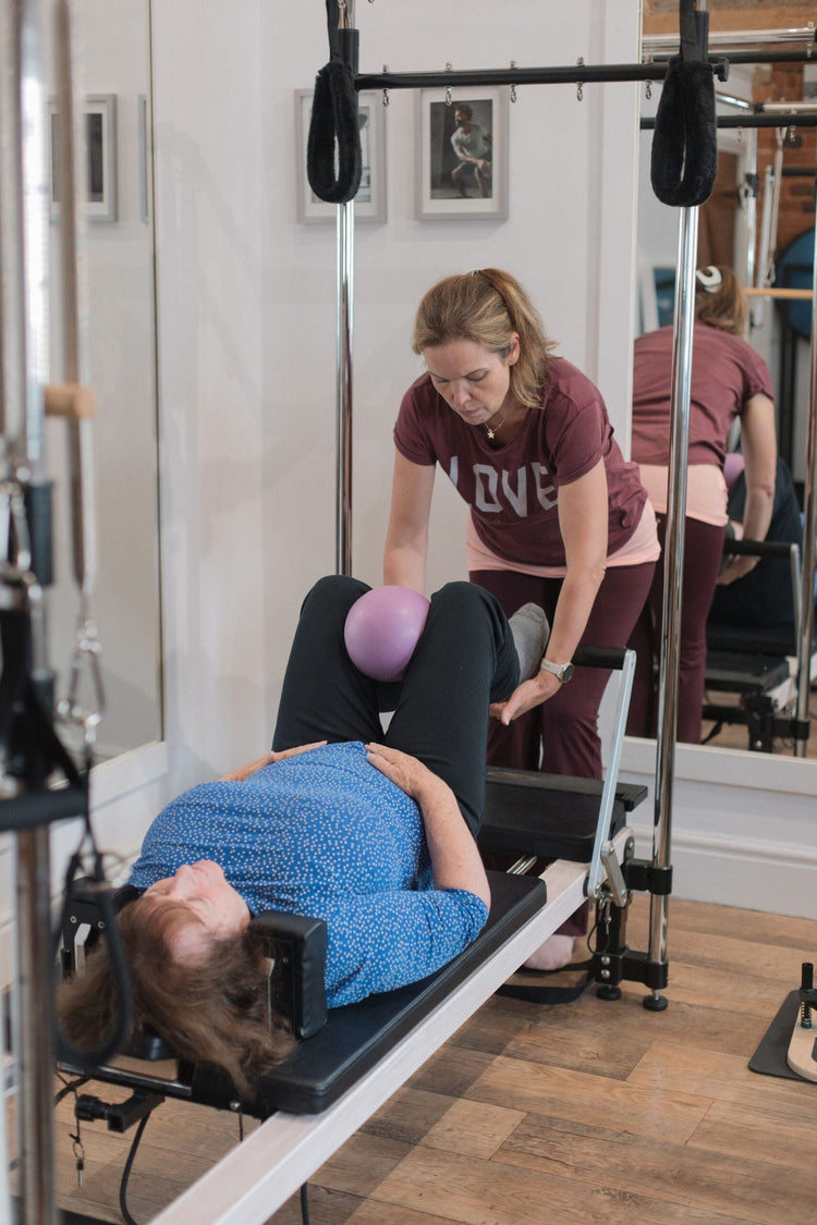 Instructor guiding a client through a gentle, joint-friendly reformer exercise with a soft ball for osteoarthritis