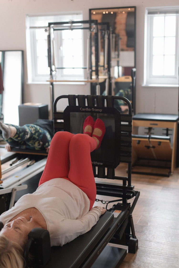 Client lying calmly with legs resting on the Cardio-Tramp, using reformer Pilates to lower stress and cortisol