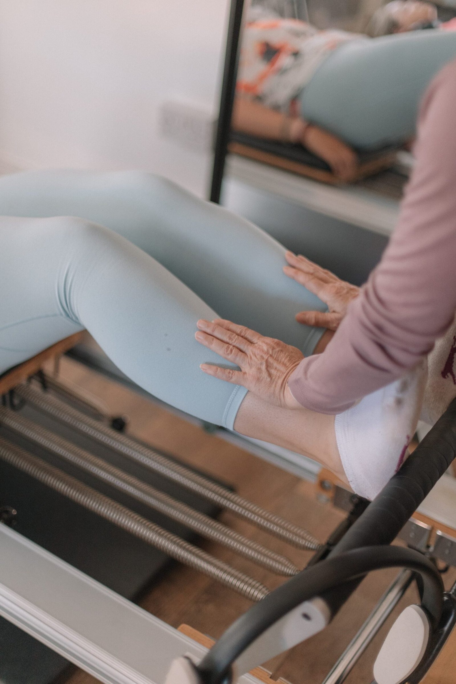 Instructor's hands checking a client's knee alignment during reformer footwork