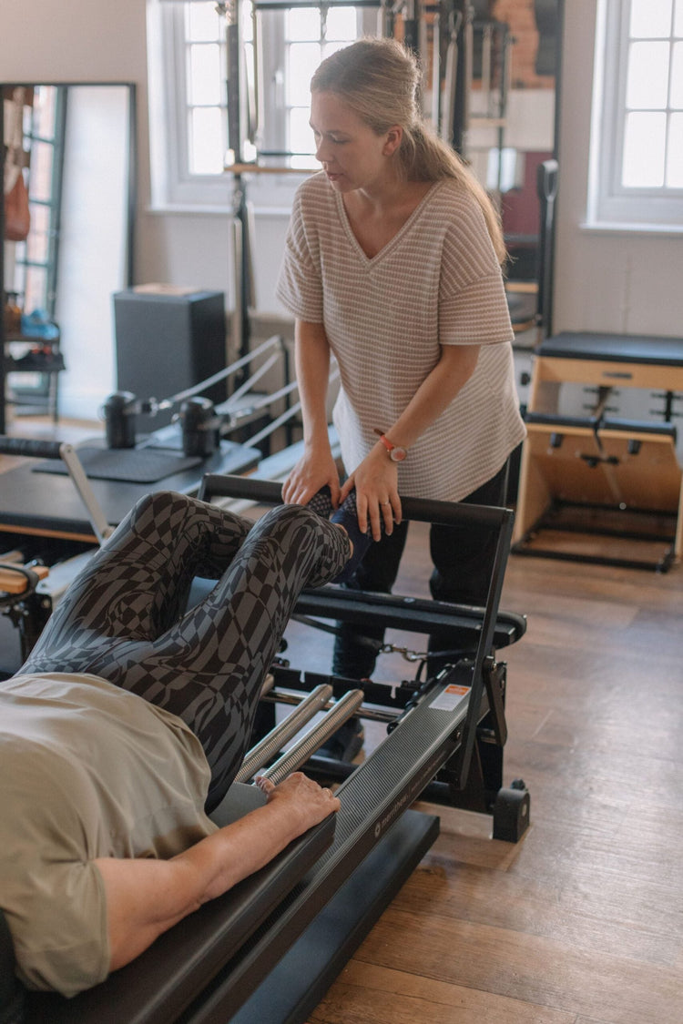 Instructor guiding a client's footwork during a one-to-one reformer session at The Old Dairy Pilates