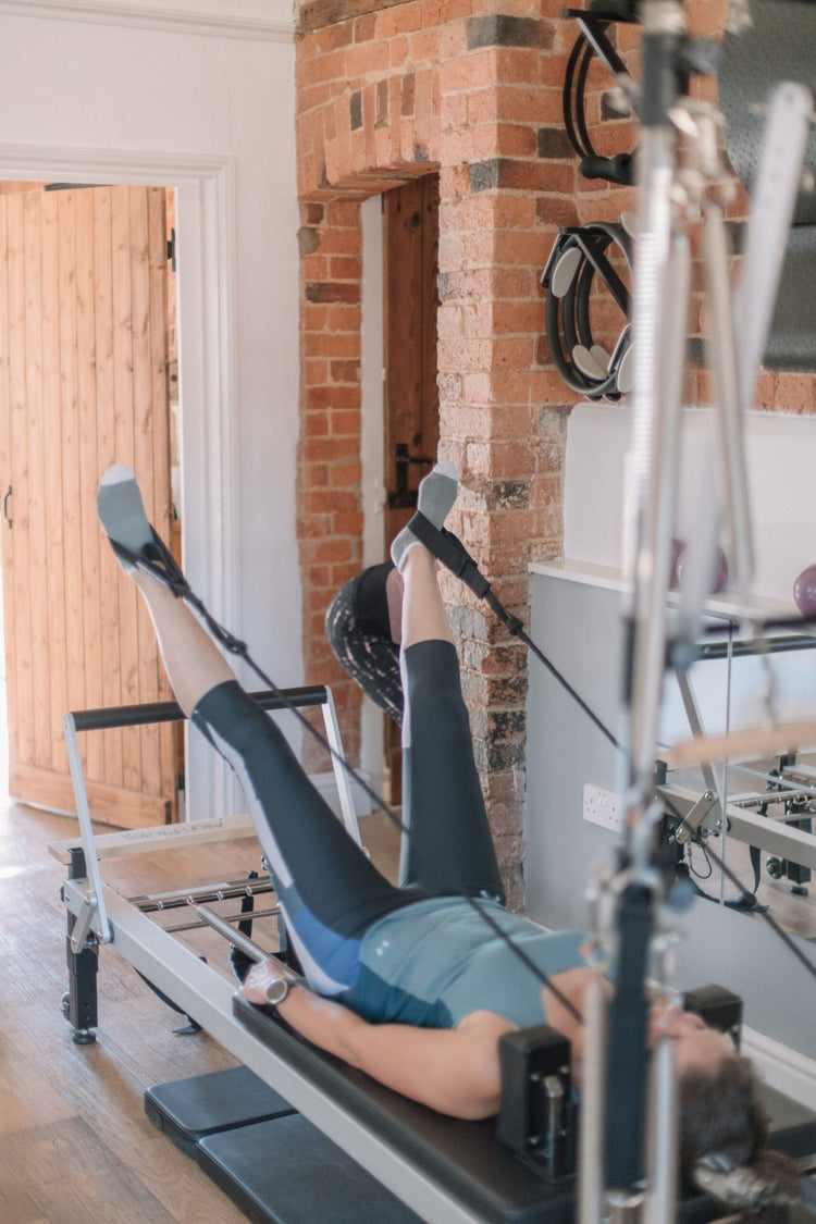 Client with legs supported in the reformer straps, a gentle position often used when working around sciatica