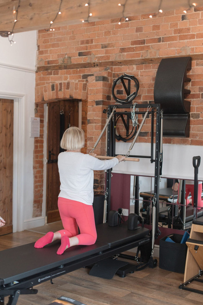 Client kneeling at the reformer tower, pulling the straps