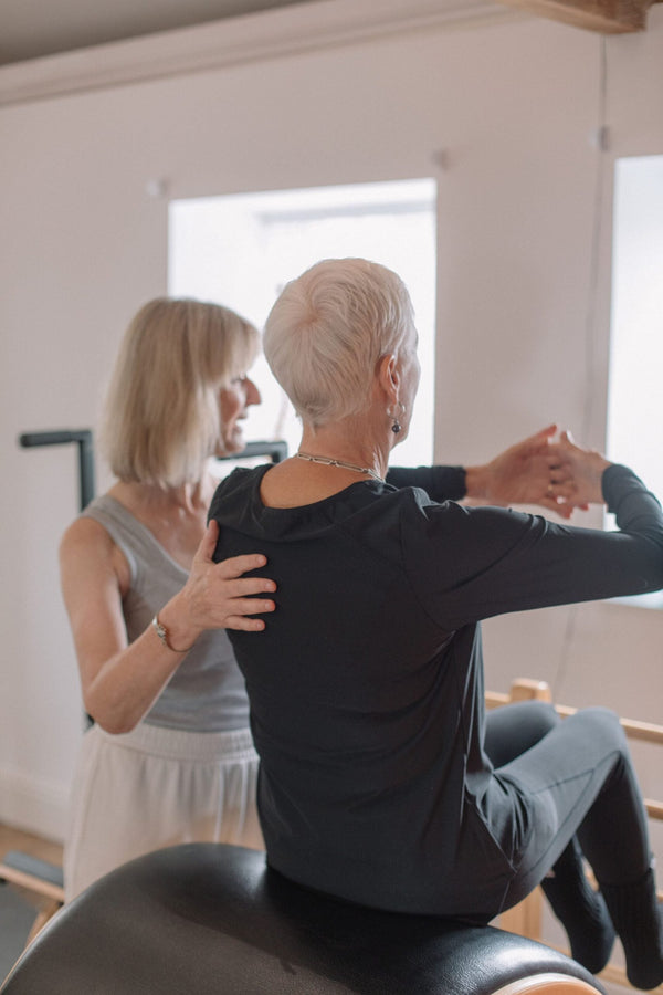 Client performing a seated twist on the ladder barrel with instructor support