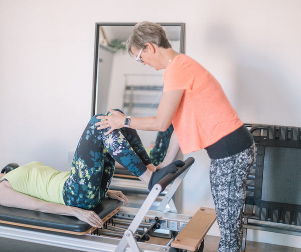 Instructor adjusting a client's leg at the reformer footbar