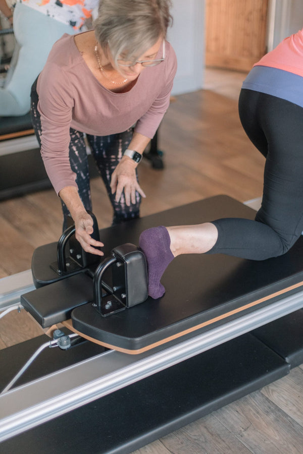Instructor guiding a kneeling client at the reformer shoulder blocks